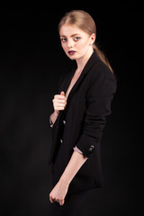 Obraz premium Beautiful fashionable blonde lady in suit on black background in studio photo. Glamour and elegance
