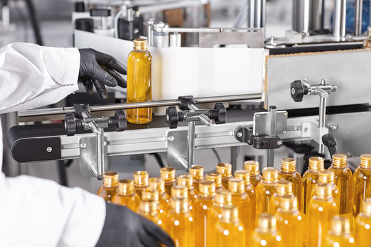Indoor portrait of factory building. Hand in black rubber gloves holding glass bottle with yellow serum putting it on conveyor. Production process of creating new shampoo. Research, development