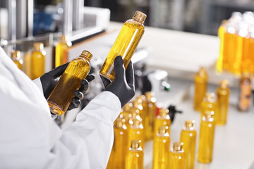 Manufacturing concept. Factory worker holding two glass bottles with yellow liquid comparing...