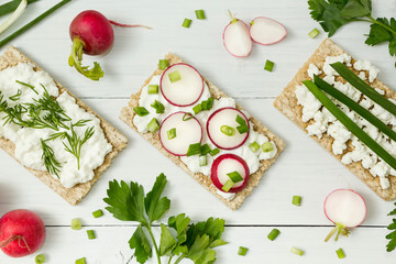 Bread slices with cream cheese, radish slices and chives on wooden board