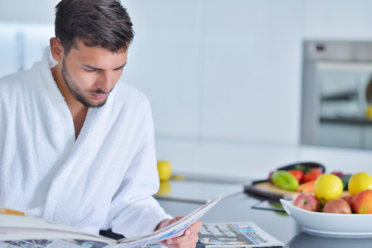 Young Man In Bathrobe Sitting On Kitchen Worktop And Having A Cup Of Tea