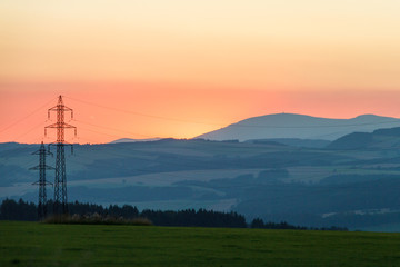 Linia energetyczna na łące o  zachodzie słońca na tle gór