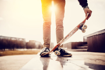 male skateboarder guy is holding a skateboard at sunset or sunrise. Concept active rest. Wipes and holes on the shoe.