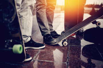 Male skateboarder man holds a skate board in his hand against the background of a team of team friends and a sunset. Concept of engaging in active and extreme sports.