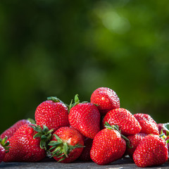 Juicy strawberries in the sun are scattered on a wooden table, against the backdrop of a beautiful background green garden. Cooking, food industry, 
restaurant business, gardening, nutrition 