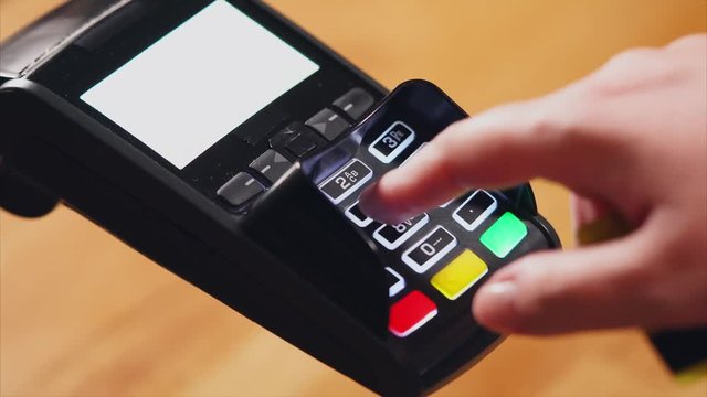 Close up shot of the process of paying a bank card account, the man's hands hold a plastic card over the terminal, then the fingers enter the pincode