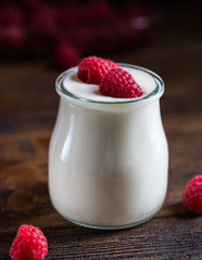 White yogurt with raspberries in glass bowl on rustic table.