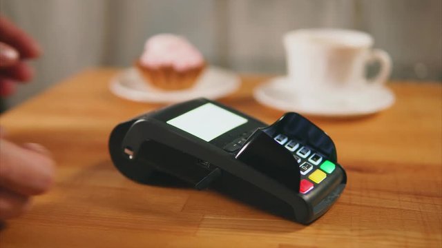 Close up shot of woman hands, who pays coffee and dessert by credit card contactless method of payment. A woman makes a transfer of funds using a terminal and a plastic card in a cafe.