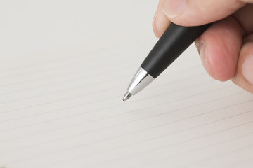 手に持たれた黒いボールペンのペン先、罫線入りのノートの背景