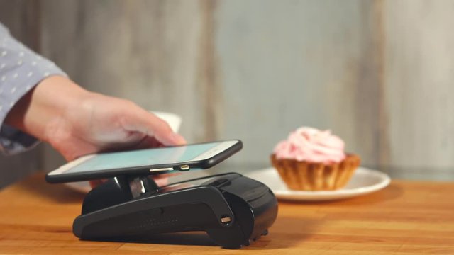 Close up shot of the contactless payment of dessert and coffee in a small cafe, a man's hands bring the smartphone to the terminal to make a purchase