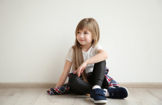 Cute little girl sitting on floor against light wall background. Fashion concept