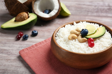 Fototapeta na wymiar Coconut rice with berries, cashew nuts, avocado and lime slices on wooden table