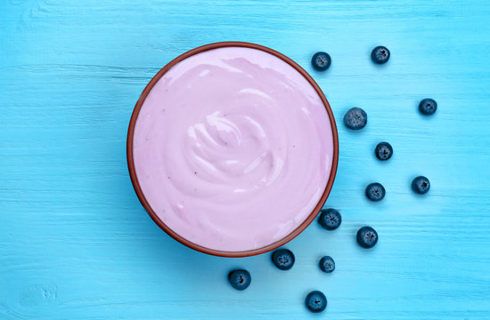 Bowl with yogurt and blueberries on wooden background