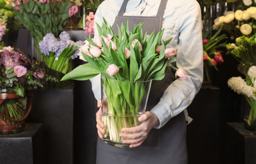 Female florist holding glass vase with tulips in flower shop
