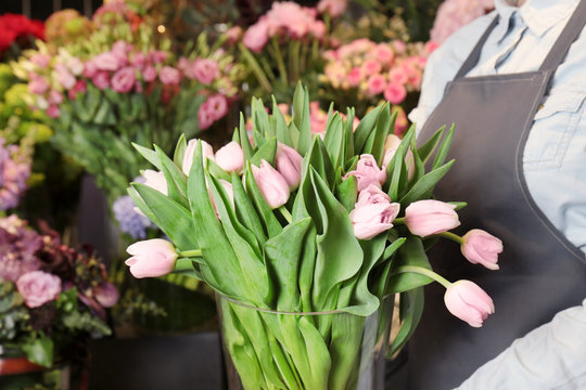 Female florist holding beautiful tulips in flower shop, close up