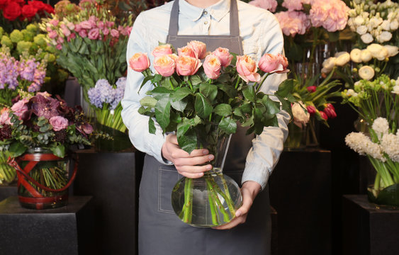 Female florist holding glass vase with roses in flower shop