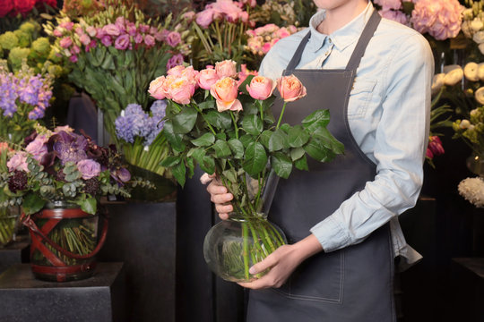 Female florist holding glass vase with roses in flower shop