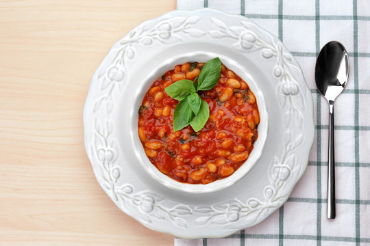 Beautiful dinnerware with delicious Italian butter beans, spoon and napkin on light wooden background
