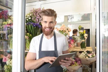 Cercles muraux Fleuriste Young handsome florist working with tablet in flower shop