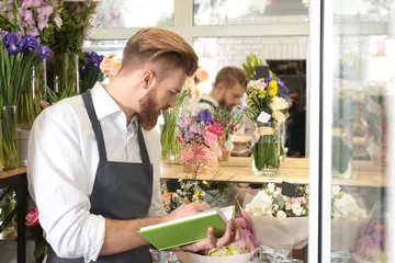 Crédence de cuisine en verre imprimé Fleuriste Young handsome florist writing in notebook at flower shop