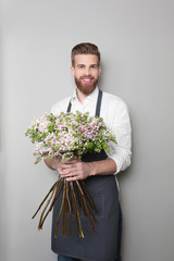 Young handsome florist with beautiful bouquet on grey background