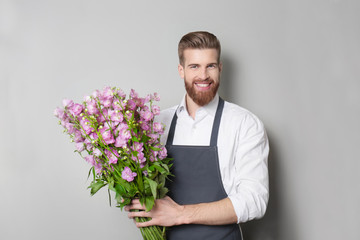Young handsome florist with beautiful bouquet on grey background