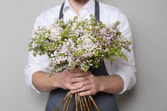 Young florist with beautiful bouquet on grey background