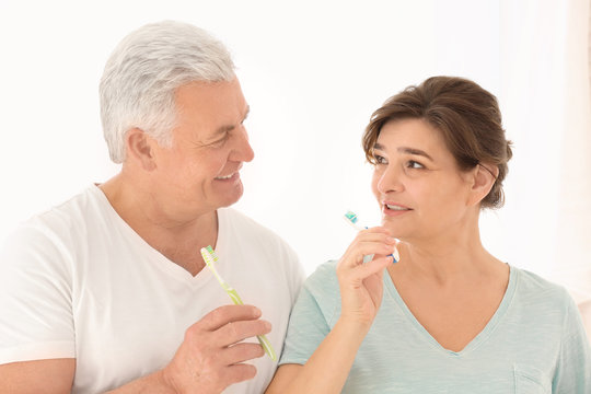 Senior couple cleaning teeth on light background