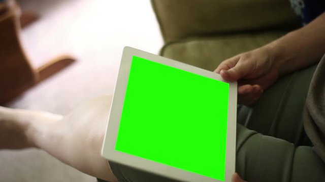 Woman watches generic green screen tablet in home living room during the day