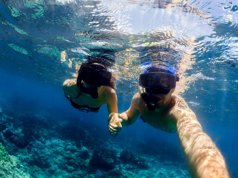 Young couple diving in clear ocean water. Honeymoon full of adventures and joy.