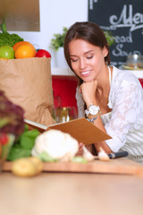 Young woman reading cookbook in the kitchen, looking for recipe