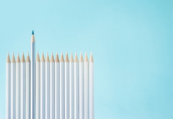 Business concept - lot of white pencils and one color pencil stand on blue paper background like fence. It's symbol of leadership, teamwork, united and communication.