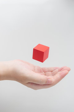Surreal design concept - Abstract geometric real wooden cube float on girl's hand with grey background.