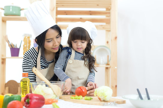 Mother and kid girl cooking and cutting vegetables on kitchen