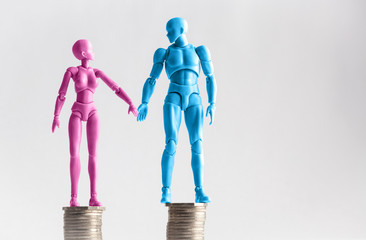 Male and female figurines holding hands looking at eachother, standing on top of equal piles of coins. Income equality concept with copy space