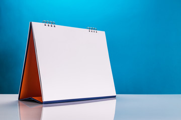 Blank paper desk calendar on table with blue background.