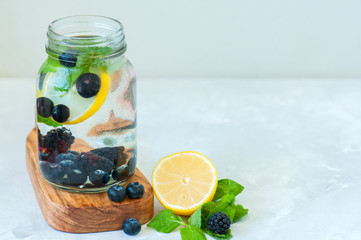 Infused detox water with lemon blackberry blueberry and mint leaves in a mason jar on a wooden board over white backgroun