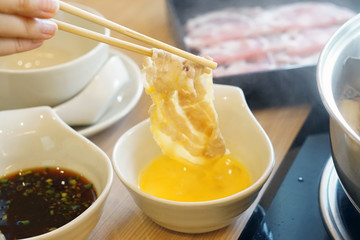 Shabu Shabu such as Sukiyaki and Hot Pot, Hand holding chopsticks with boiled kurobuta pork dip in raw beaten egg, Japanese Hot pot Style.