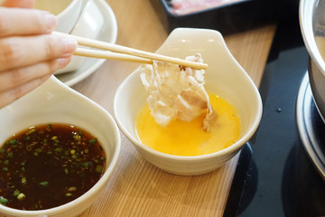 Shabu Shabu such as Sukiyaki and Hot Pot, Hand holding chopsticks with boiled kurobuta pork dip in raw beaten egg, Japanese Hot pot Style.