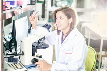 Portrait of a female researcher working in a lab scientist using microscope with colleague working in background