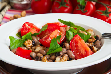 Close up of healthy and delicious salad with ripe tomatoes bean walnuts served in a plate.