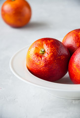 Fresh ripe blood oranges in a plate on a white stone background. Copy space and close up.