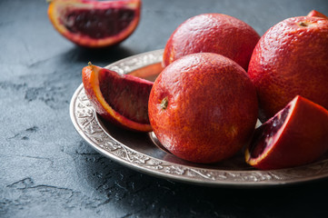 Whole and slices of blood oranges in a vintage plate on a black slate background. Copy space and...
