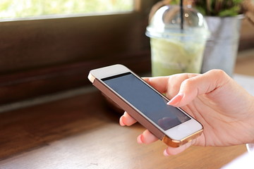 Mobile phone is held by hands of young Asian woman in coffee cafe.