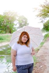 portrait asian beautiful fat woman with umbrella in the garden, relax in the garden, Large woman happy in the meadow, Woman with overweight, beautiful plus size. Asian girl with umbrella.