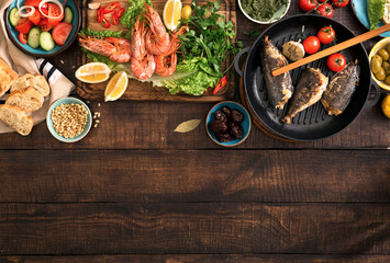 Family dinner table with shrimp, fish grilled, salad, different snacks with border, top view