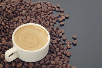 White cup of coffee with roasted coffee beans on dark table