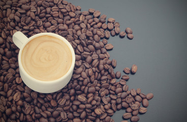 White cup of coffee with roasted coffee beans on dark table