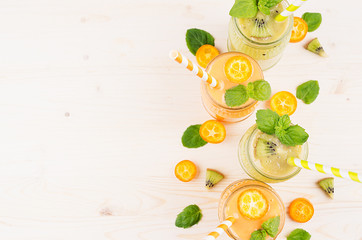 Orange kumquat and green kiwi fruit smoothie in glass jars with straw, mint leaf, cut ripe berry, top view. White wooden board background, copy space.