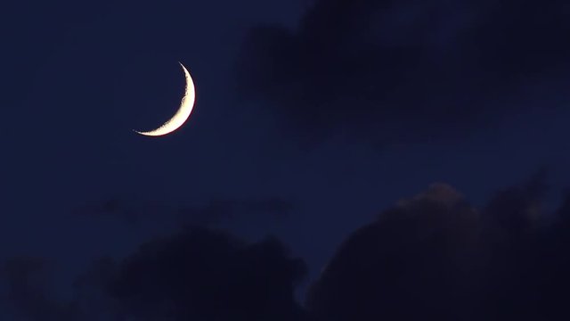 Crescent moon in night sky with approaching clouds